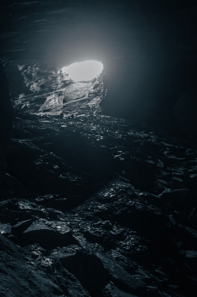 A photo of a tunnel entrance from inside a tunnel, with slate all over the floor.