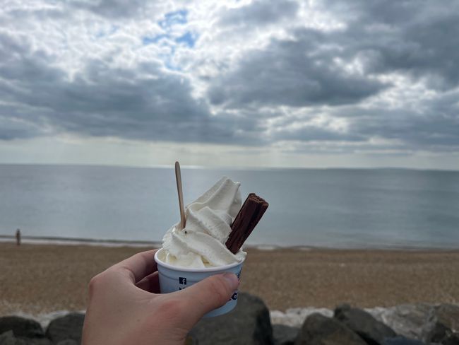 A photo of a person holding up an ice cream in front of a beach and sea