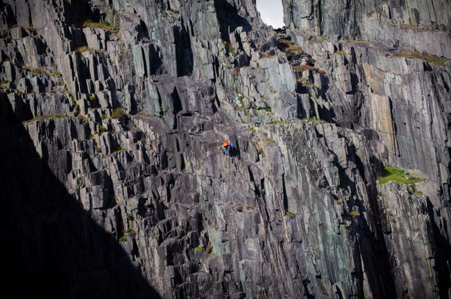 A cliff with a climber in the center with orange coat