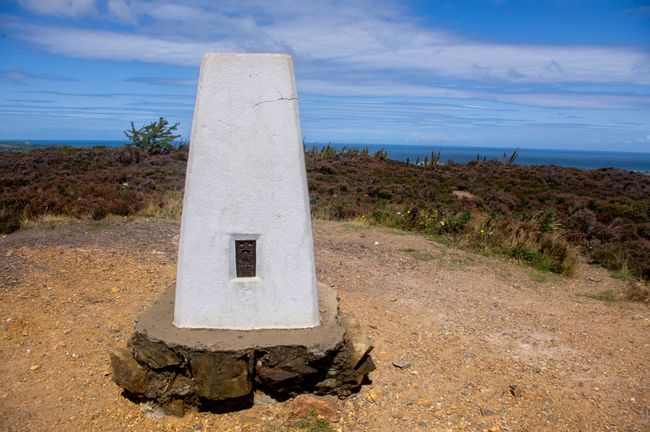 A white Ordnance Survey trig point with the sea in the background