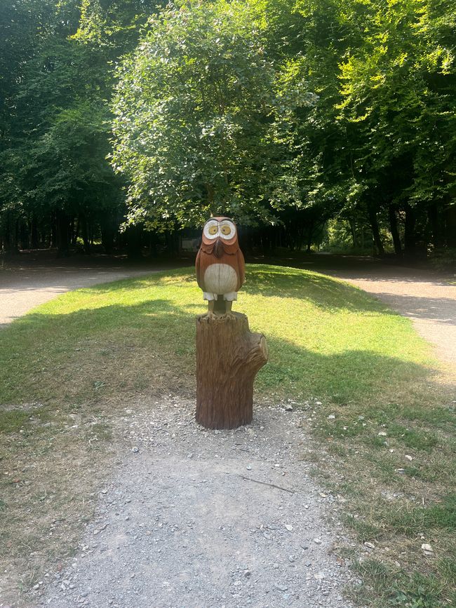 A owl carved out of wood sat amongst trees