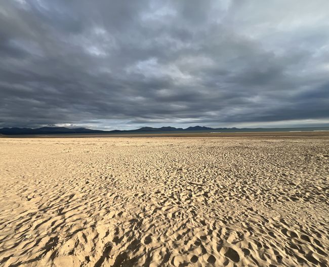 A view of sand, sea and, mountains in the distance