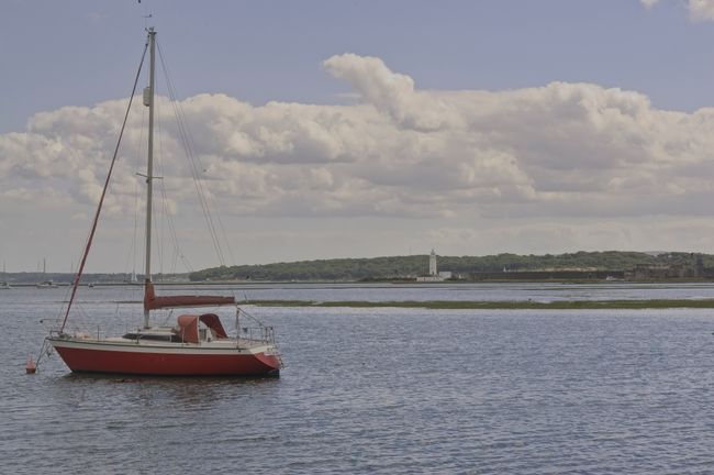 A red boat on the sea with lighthouse far in the background